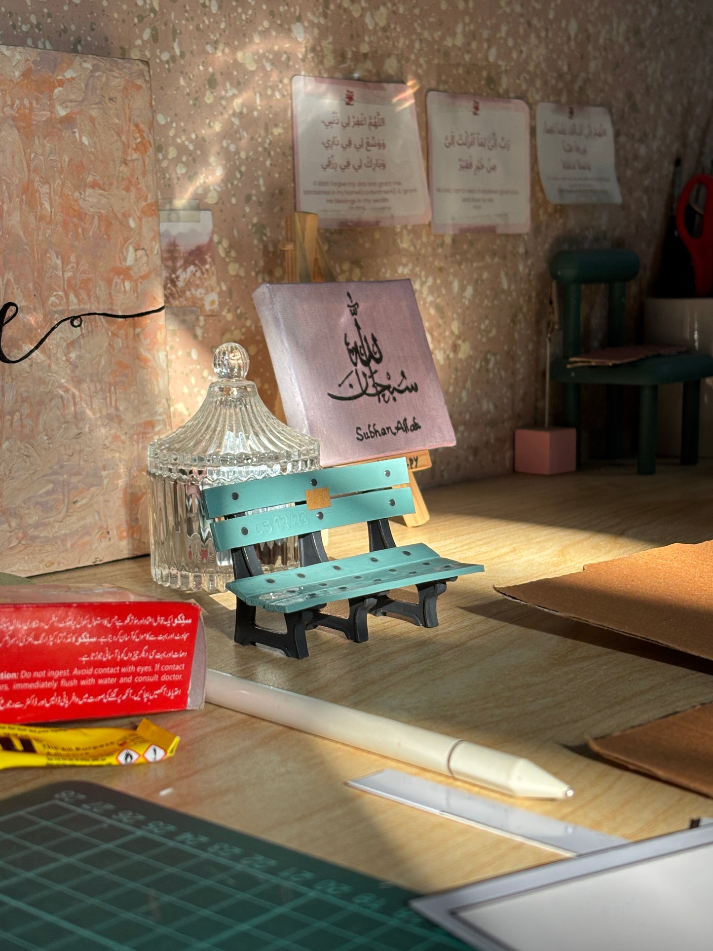 Turquoise and black miniature bench-shaped pen holder on a sunlit desk