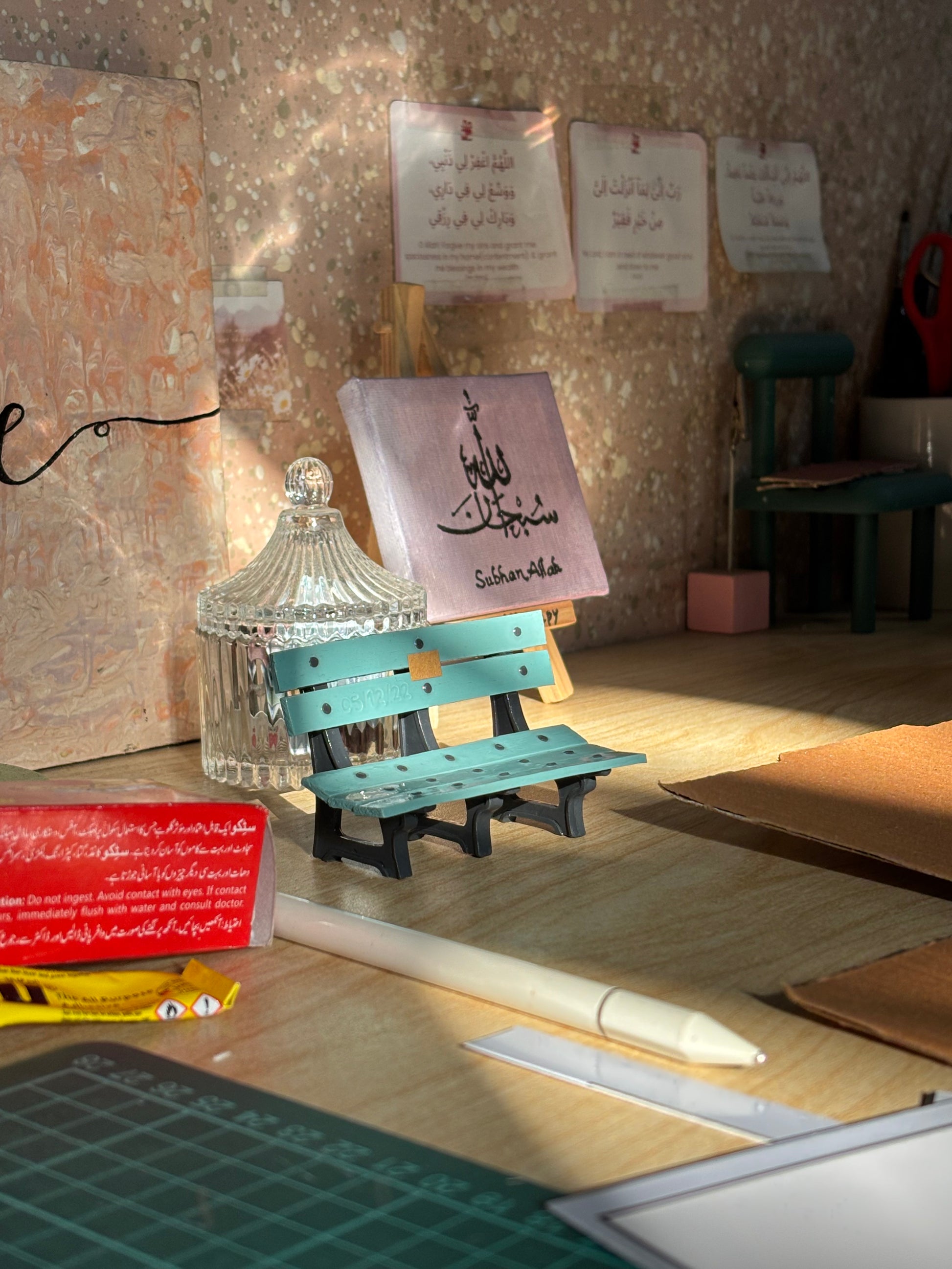 Turquoise and black miniature bench-shaped pen holder on a sunlit desk
